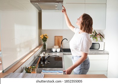 Cropped view of woman select mode on cooking hood, standing near kitchen appliance in modern interior house with house plants in flower pot on hobs. Stock photo