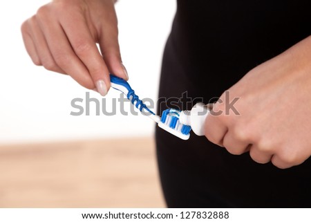 Cropped view of a woman sqeezing toothpaste from a tube onto the bristles of a plastic toothbrush