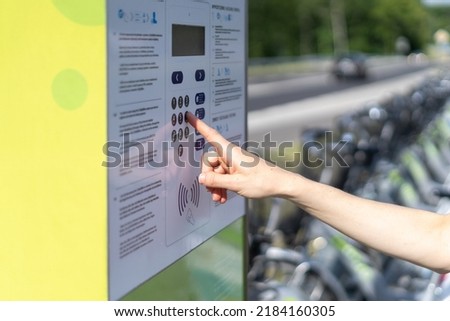 Cropped view of woman unlock rented bike, press button on parking station, choosing payment method on terminal. Bicyclist community, care about environment, alternative public transport