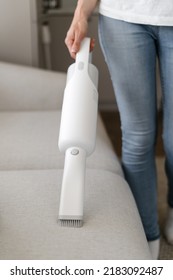 Cropped view of woman using wireless vacuum to clean sofa in living room. Concept of cleanliness. Household equipment usage. Housewife chores. Cleaning service worker