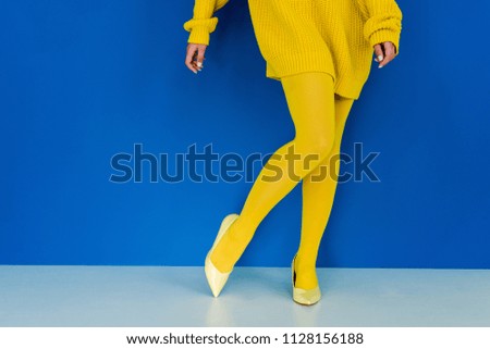 Cropped view of woman wearing yellow clothes and shoes posing on blue background