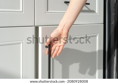 Cropped view of woman's hand opening white wood cupboard door. Contemporary kitchen furniture concept. New luxury apartment details. Cabinet usage