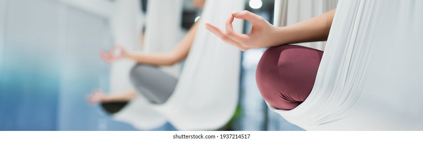 cropped view of women meditating in lotus pose in aerial yoga hammocks, blurred background, banner