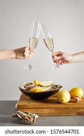 cropped view of women toasting champagne glasses with sparkling wine near bowl with oysters and fresh lemons isolated on grey 