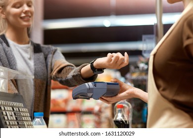 Cropped view of young adult consumer paying for shopping with contactless technology on modern smart watch while cashier holding terminal in hand