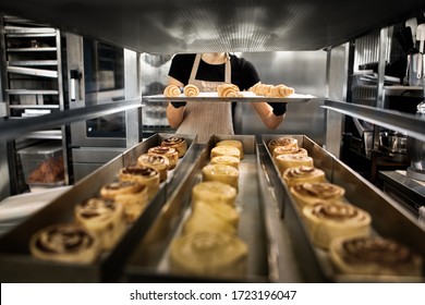 Cropped view of young adult female working on kitchen in bakery patisserie, holding tray with raw pastry in hands, preparation to cooking fancy bread - Powered by Shutterstock
