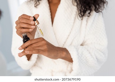 Cropped View Of Young African American Woman Holding Bottle And Pipette With Serum Essential Oil In Hands, Applying Liquid On Soft Skin. Skincare And Natural Organic Cosmetics Concept