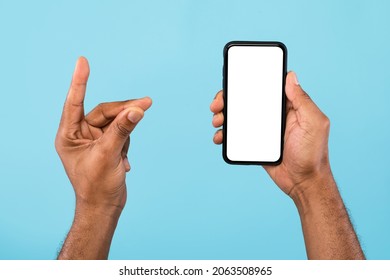 Cropped View Of Young Black Guy Showing Smartphone With Empty White Screen And Holding Something On Blue Background, Mockup For Mobile App, Website And Business Card Design