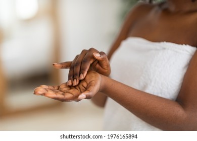 Cropped view of young black woman applying moisturizing hand cream at home, closeup. Millennial African American lady wearing white towel, pampering her skin after shower or bath
