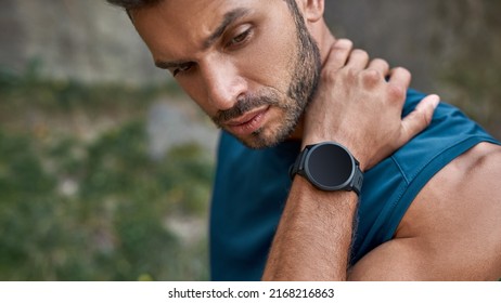 Cropped view of young caucasian sportsman thinking about something outdoors. Handsome bearded athletic man wearing sportswear and smartwatch. Concept of modern healthy lifestyle. Warm summer day