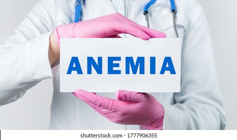 Cropped View Of Young Female Doctor In A White Coat And Pink Sterile Gloves Holding A Card With Text ANEMIA. Medical Concept.