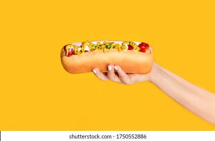 Cropped view of young girl holding yummy hot dog with mustard and ketchup on orange background