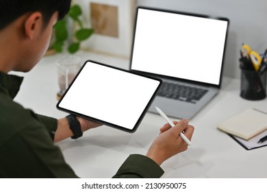 Cropped View Young Man Sitting In The Office Working On A Touchscreen On A Tablet And A Laptop With Blank White Screens, For Business And Technology Concept.