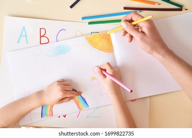 Cropped view of young mother and her little child girl sitting behind desk, drawing on white paper together, using colorful pencils - Shutterstock ID 1699822735