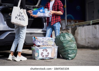 Cropped View Of The Young Open Minded Family Unpacking Bags And Plastic Containers With Rubbish From Their Electro Car Before The Visit To The Garbage Sorting Factory. Garbage Recycling Concept