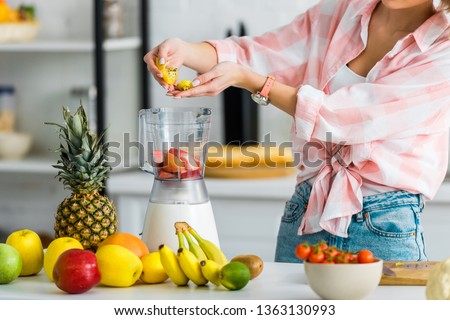 cropped view of young woman adding ingredients in blender  near fruits