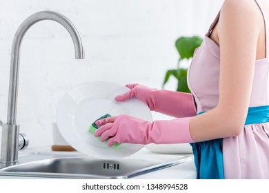 cropped view of young woman in pink rubber gloves washing dishes in kitchen - Powered by Shutterstock