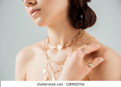 cropped view of young woman with shiny lips in golden necklaces and rings isolated on grey