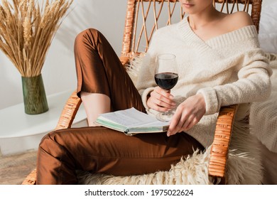 cropped view of young woman sitting in rocking chair with book and glass of wine - Powered by Shutterstock