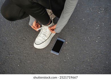 cropped woman in squat position tying shoelace with blank screen phone - Powered by Shutterstock