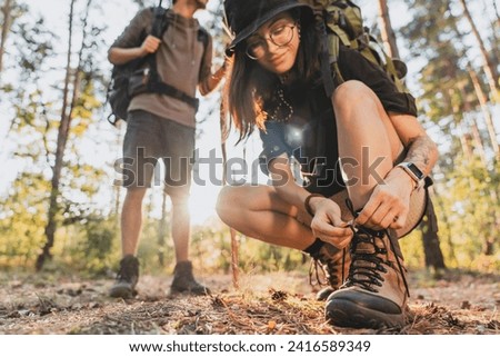 Cropped of woman tying hiking boot outdoors on trail in forest while travel with her boyfriend. Caucasian couple in mountains woods, walking spending time holidays in summer