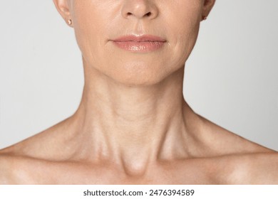 Cropped of a womans neck and chin. The woman is wearing a light color shirt and has a neutral expression. Her skin is smooth and wrinkle-free.