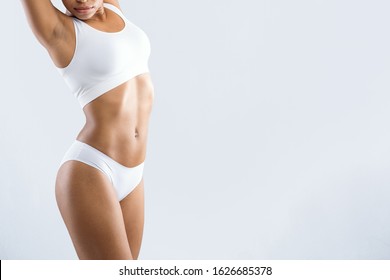 Cropped of young afro woman in white underwear showing her beautiful body over grey studio background with empty space, slimming concept
