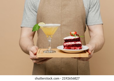 Cropped Young Man Barista Barman Employee Wears Brown Apron Working In Coffee Shop Hold Martini Cocktail Cake Dessert Isolated On Plain Pastel Light Beige Background. Small Business Startup Concept