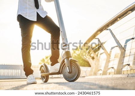 Cropped of young man getting ready for riding on electric scooter through city. Closeup male legs driving e-transport outdoors