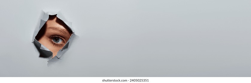 cropped young woman with blue eye looking at camera through hole in ripped grey paper, banner - Powered by Shutterstock