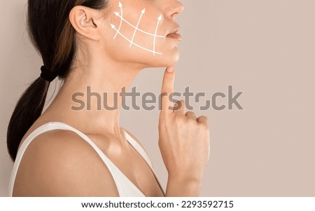 Cropped of young woman with clean fresh skin touching her chin, antiaging concept. Side view of unrecognizable lady in white top with lifting arrows on cheek, beige studio background, copy space