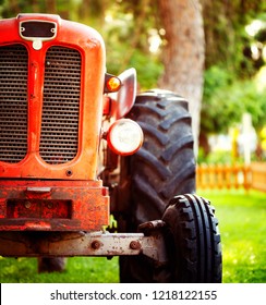 Croppped Photo Of Old Vintage Red Tractor Standing On A Farm Field At Sunset.