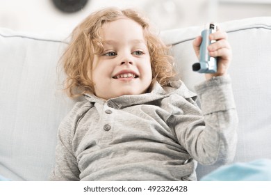 Croppped shot of a beautiful child resting on a couch and holding an inhaler in his hand - Powered by Shutterstock