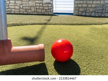 Croquet on a cruise ship. A croquet mallet strikes a red croquet ball on green artificial turf. 