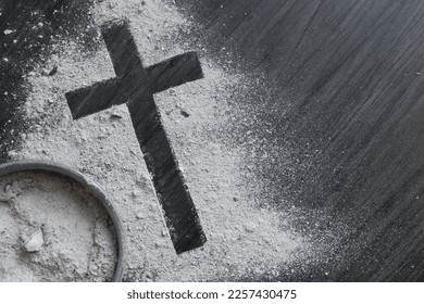 Cross of ashes and bowl filled with ashes on a dark wood background with copy space 