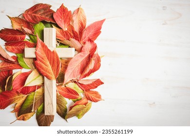 Cross with autumn leaves on a white background with copy space 