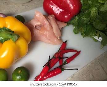 Cross contamination, different types of vegetables such as bell peppers, onion, chili, lime, mint on the same white chopping board with raw chicken