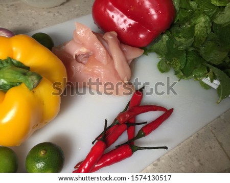 Cross contamination, different types of vegetables such as bell peppers, onion, chili, lime, mint on the same white chopping board with raw chicken