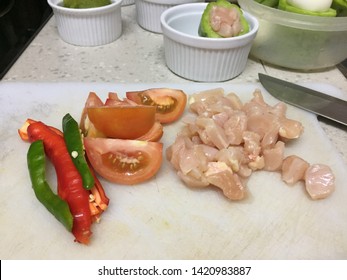 Cross contamination of food, chicken and vegetables such as tomato and chilies are on the same white chopping board - Shutterstock ID 1420983887