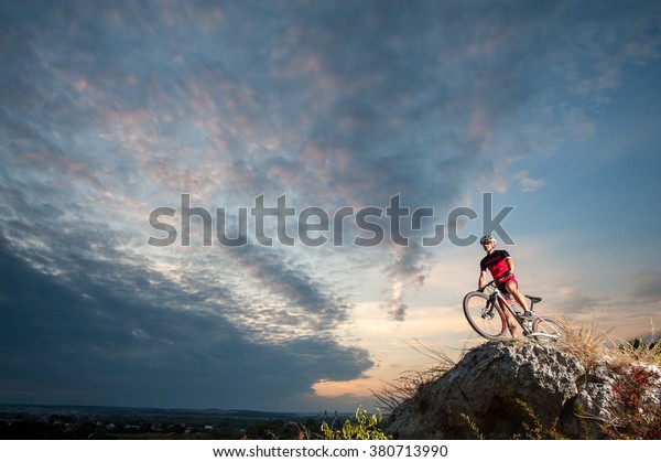 cross country biker\
relaxing on the top of the mountain, enjoying beautiful sunset on\
overview point.