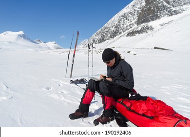 Cross Country Skier Sitting On Her Pulka And Looking At A Map.