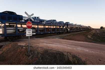 A Cross Country Train Slowly Heading Toward Perth From South Australia Carrying People, Vehicles And Other Freight At A Rural Railway Crossing.