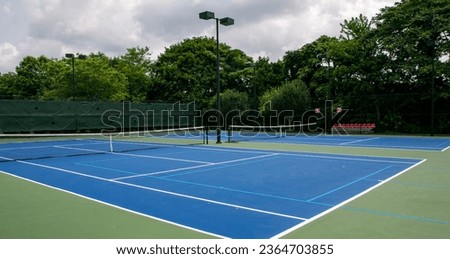 Cross court view of pickleball tennis courts painted blue and green with lights and trees in the background.