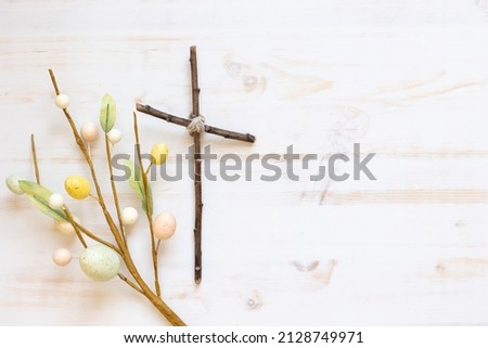 Cross with decorative branch with easter eggs on a white wood background with copy space