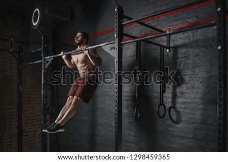 Cross fit athlete doing pull-ups at the gym. Practicing calisthenics. Handsome man doing functional training. 
 