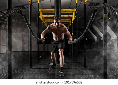 Cross fit training. Man working out with battle ropes at gym 