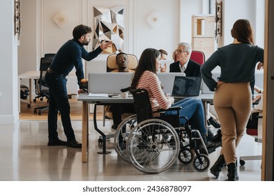 A cross generational group of professionals engage in a business meeting. The image includes a person using a wheelchair, depicting inclusivity and teamwork in a modern office setting. - Powered by Shutterstock