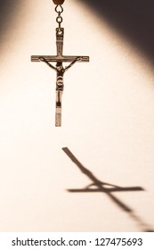 Cross Hanging From Rosary Beads Casting A Shadow