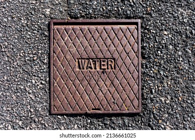 Cross Hatched Rusty Metal Water Value Cover In A Tarmac Pavement