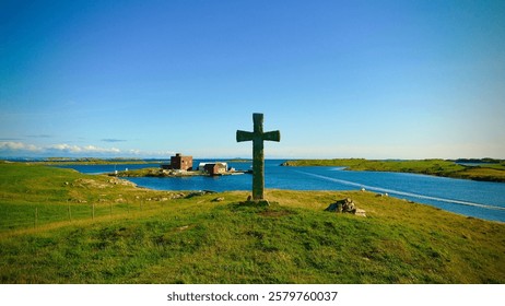 A cross with a rustic brown finish, surrounded by vibrant green grass, is standing in the center of a shimmering body of water